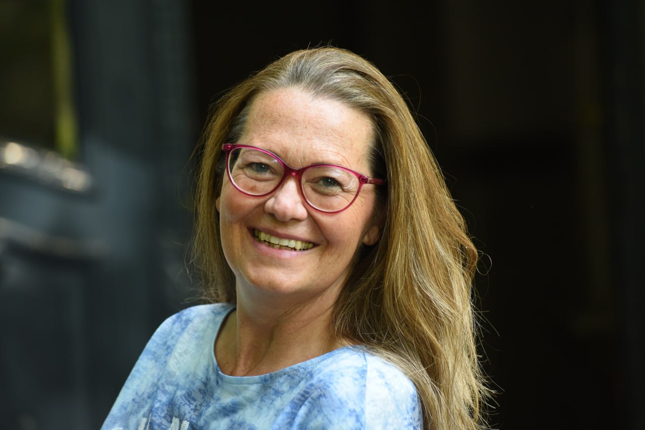 Frau mit Brille und blauem Shirt, die ein herzliches Lächeln zeigt.