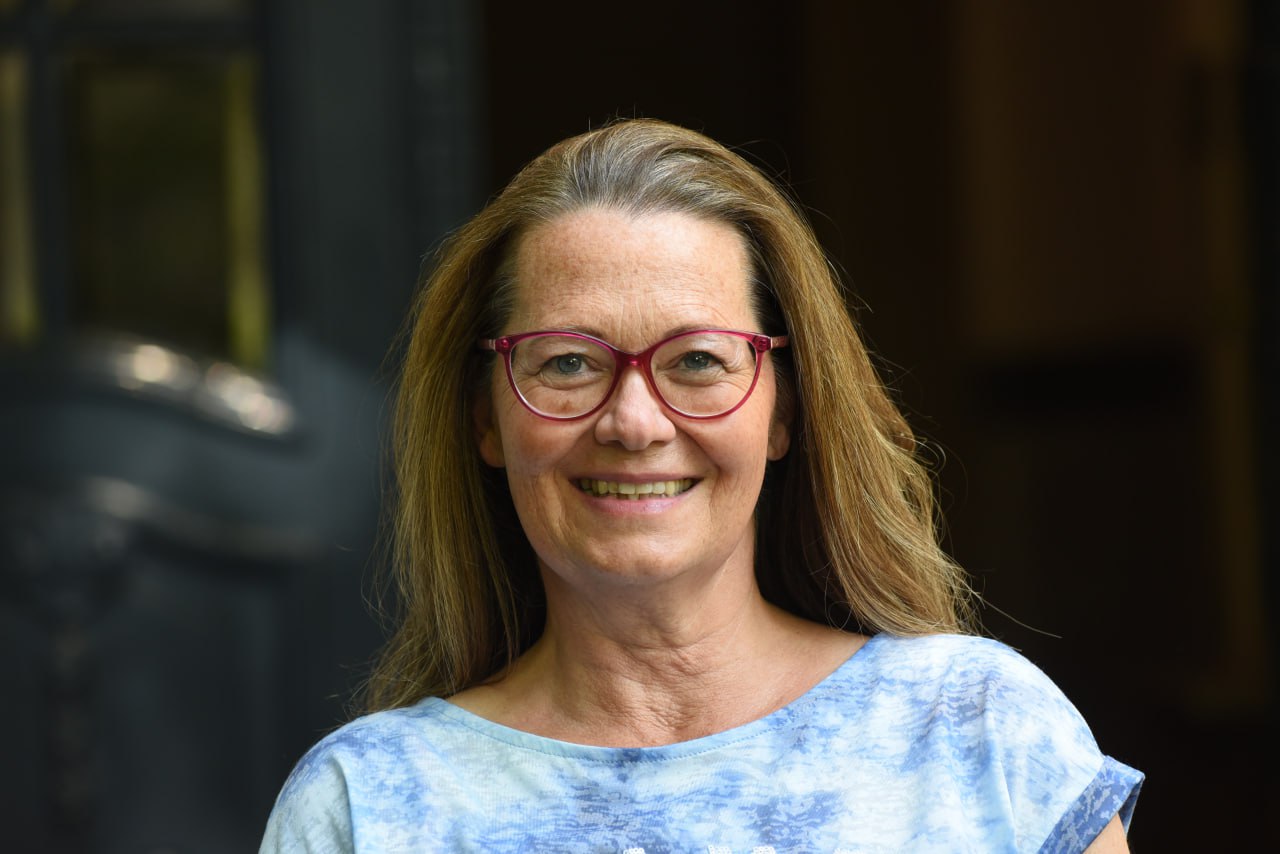 Frau mit Brille und blauem Shirt lächelt freundlich in die Kamera.